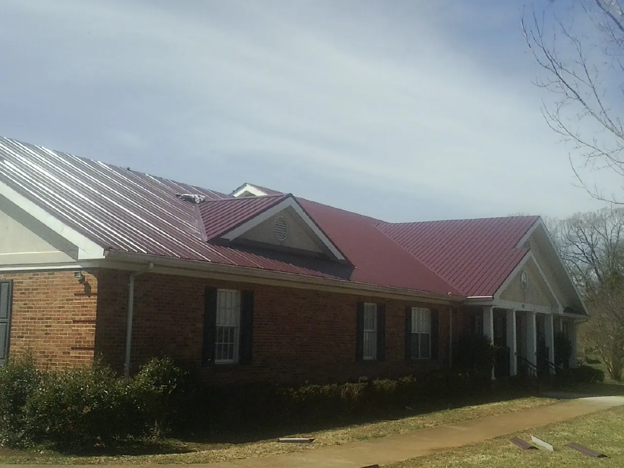 Red metal roof with gabled entries on a long brick building, from a Hail Damage Roof Repair job in Vashon