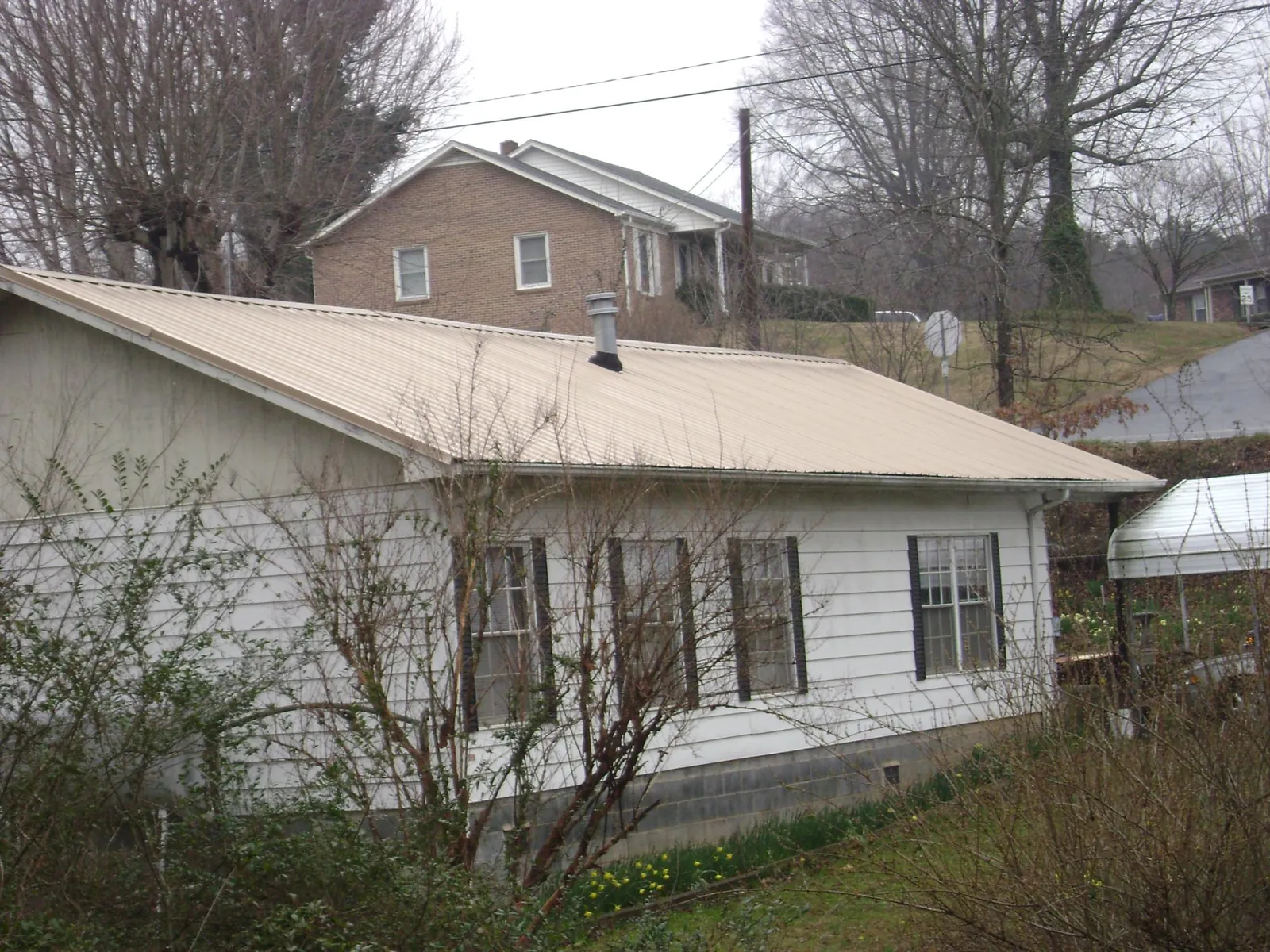 Tan metal roof on a white sided house set into a hillside — Commercial Roofing by Roofing Brothers in Vashon